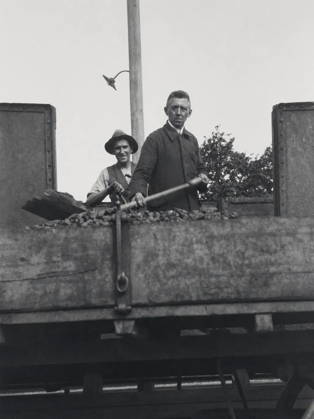 Zwei Männer mit Schaufeln bei der Arbeit auf einem historischen Kohlenwagen
